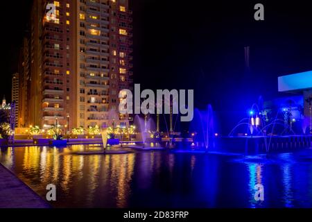 Night Cityscape with Dazzling Colorful Fountains and Illuminated Skyscraper. Stock Photo