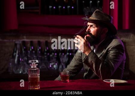 Handsome bearded man enjoying whiskey in bar. Hipster with beard drinking a brandy in bar. Brutal guy drinking alcohol. Stock Photo