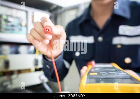The positive end of the multimeter held by an engineer with a blurred background, the concept of using digital tools to check electrical and electroni Stock Photo