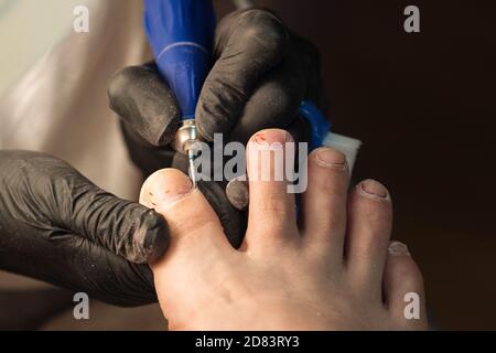 Hardware pedicure, preparation of the nail plate for applying gel polish. Master chiropody shapes the nails . Female patient in the process of hardware pedicure procedure. Foot care Stock Photo