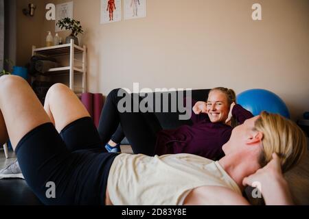 Smiling patient and physio-therapist practising crunching techniques for core stability practising in exercise studio Stock Photo