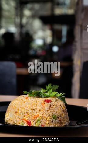 Typical oriental dish of sautéed rice with chicken and vegetables on the restaurant table. vertical image. Selective focus. Stock Photo