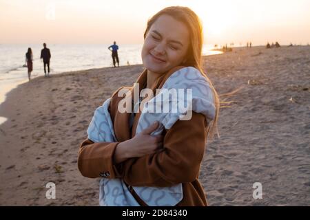Young beautiful woman wrapped up in a warm blanket, warm and cozy on the beach. Running on the beach at sunset, feeling free and happy. Stock Photo