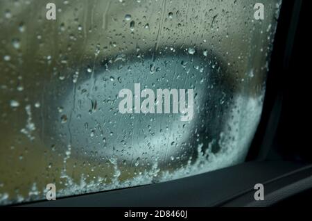 close up of fogged up car mirror looking through car window with snow and water droplets on glass in bad weather conditions in winter Stock Photo