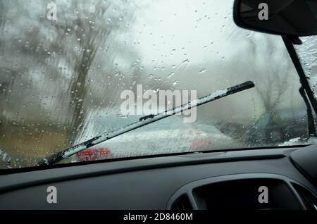 close up of car windshield wiper with snow on and dashboard. looking through windscreen  with raindrops and car infront Stock Photo