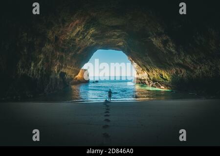 Single man in cave looking into the ocean Stock Photo