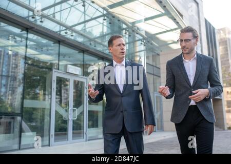 Two businessmen walking outside business center, having conversation Stock Photo
