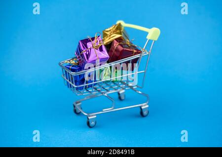 Shopping cart full of minimal present boxes. Gifts for holiday on blue background Stock Photo