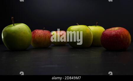 Three ripe fresh green apples and tree red apples on black table and dark background. Free copy space. School snacks or organic food concept Stock Photo
