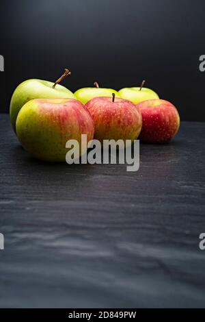 Three ripe fresh green apples and tree red apples on black table and dark background. Free copy space. School snacks or organic food concept Stock Photo