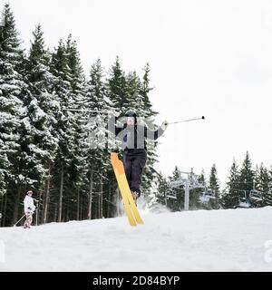 Male skier skiing on fresh powder snow with snowy pine trees on background. Man freerider holding ski poles and making jump while sliding down snow-covered slopes. Concept of extreme winter sport Stock Photo