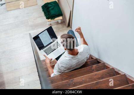 young man with a laptop sitting on the steps in his apartment. Stock Photo