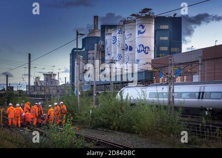 Network Rail track workers busy on the West Coast Main Line at Warrington Bank Quay station with the Unilever soaps factory in the early evening.