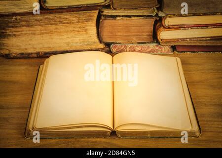 Ancient open book with empty pages on a wooden table in front of a pile of old weathered books Stock Photo