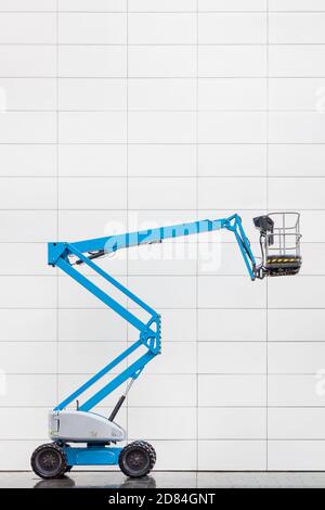 Side view of a modern blue hydraulic lift platform in front of a white tiled office wall Stock Photo