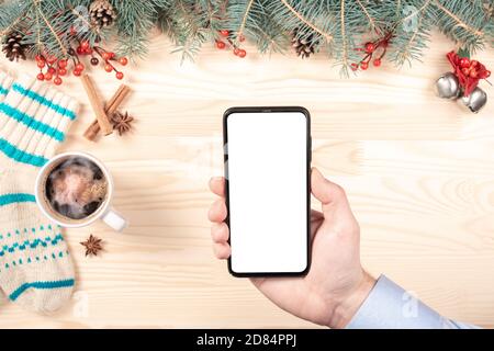 Modern cellphone with white blank screen in woman hands. Mobile phone mockup in woman hands. Christmas and new year decorations on blurry background. Stock Photo