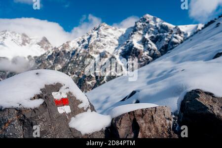 Trail marker in the mountains on the hiking trail. White and red way marker sign painted on a rock in with Alps mountains in the background Stock Photo