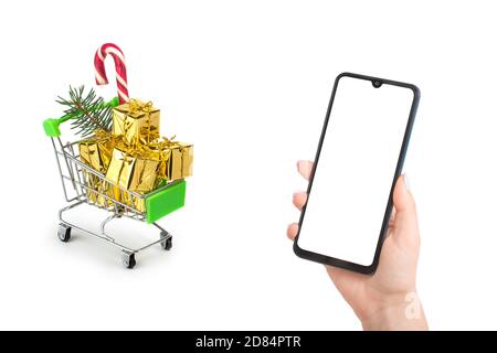 Christmas online shopping mockup. Woman's hand holds a phone with an empty white screen against the background of a gift cart. isolated on white backg Stock Photo