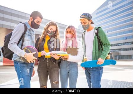Group of multiracial students in protective masks discuss past lessons outside a college on the street - Happy friends wearing face protective masks a Stock Photo