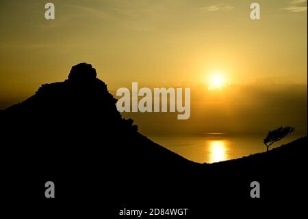A golden sunset across the sea with the sun reflecting in the water with a mountain on the left hand side in the Valley of Rocks, Exmoor, Devon Stock Photo