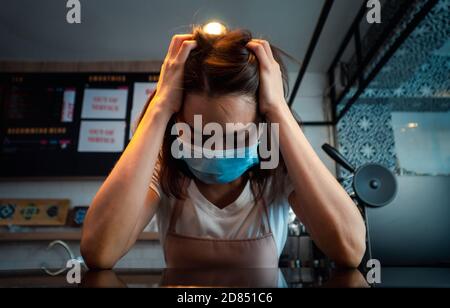 Asian woman coffee shop business owner Stressed and disappointed from The effects of the coronavirus pandemic resulting in business losses Stock Photo