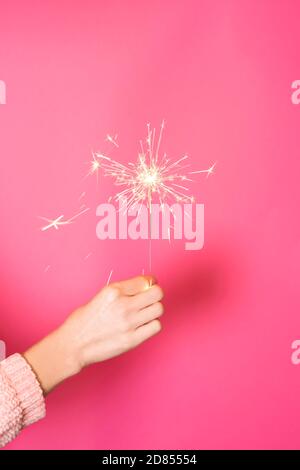 Close up of female hand with burning Christmas sparkler on pink background. Happy New Year celebration concept Stock Photo