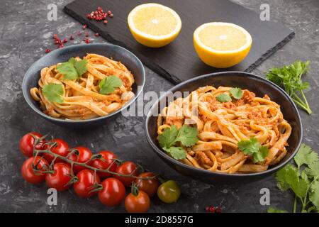 Semolina pasta with tomato pesto sauce, orange and herbs in bowls on a black concrete background. Side view, close up. Stock Photo
