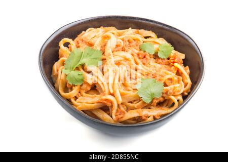 Semolina pasta with tomato pesto sauce, orange and herbs in bowl isolated on white background. Side view, close up. Stock Photo