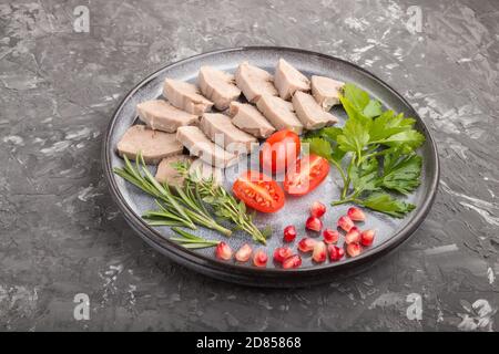 Boiled pork tongue with tomatoes and herbs on a black concrete background. Side view, close up. Stock Photo