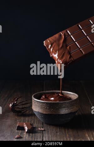 Dripping melted chocolate bar into ceramic bowl on dark background Stock Photo