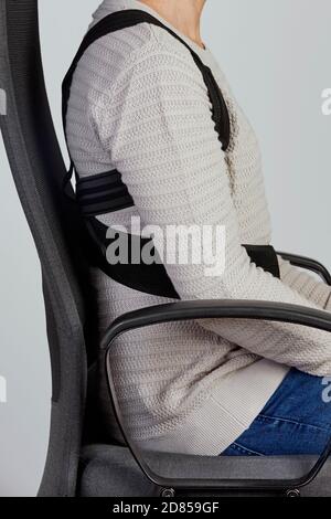 closeup of a young caucasian man wearing an upper back posture corrector as is sitting at his office chair Stock Photo