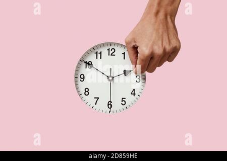 closeup of the hand of a young caucasian man setting a clock backward or forward, at the end or at the beginning of the summer, on a pink background Stock Photo