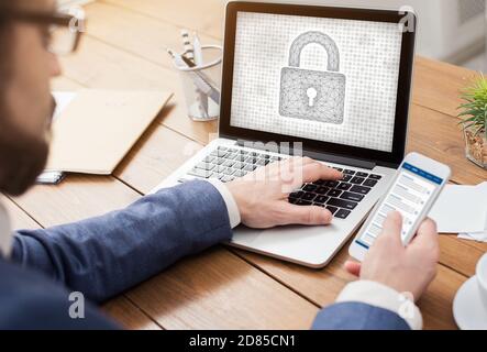 Man typing on laptop keyboard with padlock icon, holding phone Stock Photo