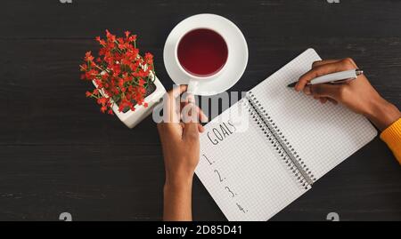 African Woman Setting Goals Writing List In Notebook Indoors, Above-View Stock Photo