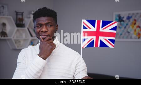 Young thoughtful black man holding UK flag considering migration for work. High quality photo Stock Photo