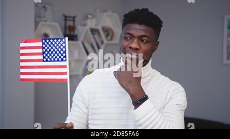 Young thoughtful black man holding usa flag. Asylum seeker thinking about job opportunities in USA. High quality photo Stock Photo