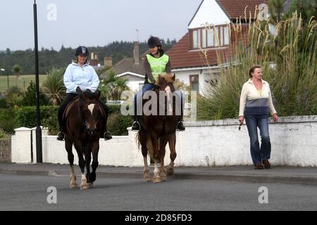 Maidens Harbour, South Ayrshire, Scotland, UK . Maidens is a village in the Kirkoswald parish of Ayrshire, Scotland. Situated on the coast of the Firth of Clyde at the southern end of Maidenhead Bay, a series of rocks known as the 'Maidens of Turnberry' form a natural harbour.  Two horse riders on the prmenade head back to the riding school Stock Photo