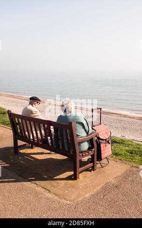 Couple sitting and chatting on a wooden bench facing the sea at Budleigh Salterton early one spring day, East Devon, England. Stock Photo