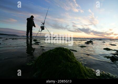 Croy Shore, Croy Bay, Carrick, Ayrshire, Scotland, UK.As the sunset over the Firth of Clyde on the West Coast of Scotland a fisherman sets his rod and line up for an evening of sea fishing. July 2012 Stock Photo