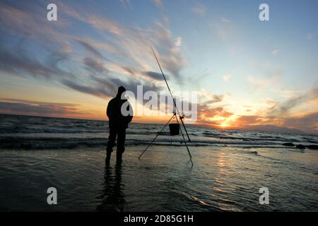 Croy Shore, Croy Bay, Carrick, Ayrshire, Scotland, UK.As the sunset over the Firth of Clyde on the West Coast of Scotland a fisherman sets his rod and line up for an evening of sea fishing. July 2012 Stock Photo