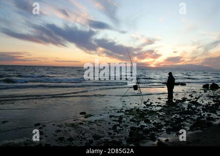 Croy Shore, Croy Bay, Carrick, Ayrshire, Scotland, UK.As the sunset over the Firth of Clyde on the West Coast of Scotland a fisherman sets his rod and line up for an evening of sea fishing. July 2012 Stock Photo