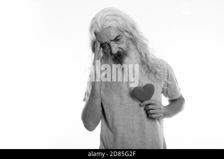 Studio shot of senior bearded man holding heart while having headache Stock Photo