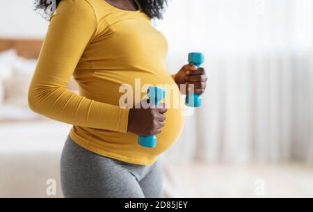 Pregnant woman lifting dumbbells, exercising at home Stock Photo