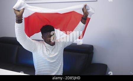 Young happy black man man with polish flag watching footbal game on tv. High quality photo Stock Photo
