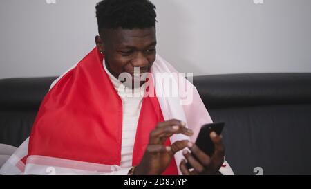 Young happy black man with polish flag watching game streaming on the smartphone. High quality photo Stock Photo