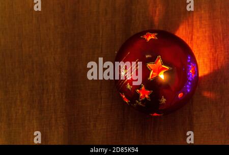 Christmas lantern ball with a lit candle inside letting light out through the star shapes on a wooden background. Top view Stock Photo