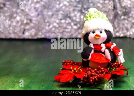 Christmas doll, penguin with wool hat on a Christmas flower on a green wooden table on a luminous background with copyspace Stock Photo
