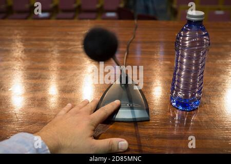 Speaker finger is about to press on-off button of a table conference microphone. Selective focus Stock Photo