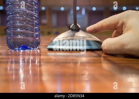 Speaker finger is about to press on-off button of a table conference microphone. Selective focus Stock Photo