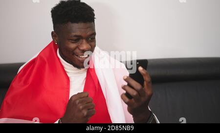 Young happy black man with polish flag watching game streaming on the smartphone. High quality photo Stock Photo